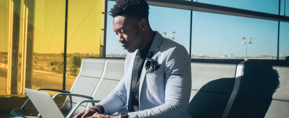 A man on a bench, engaged with his laptop, immersed in work amidst a peaceful airport setting.