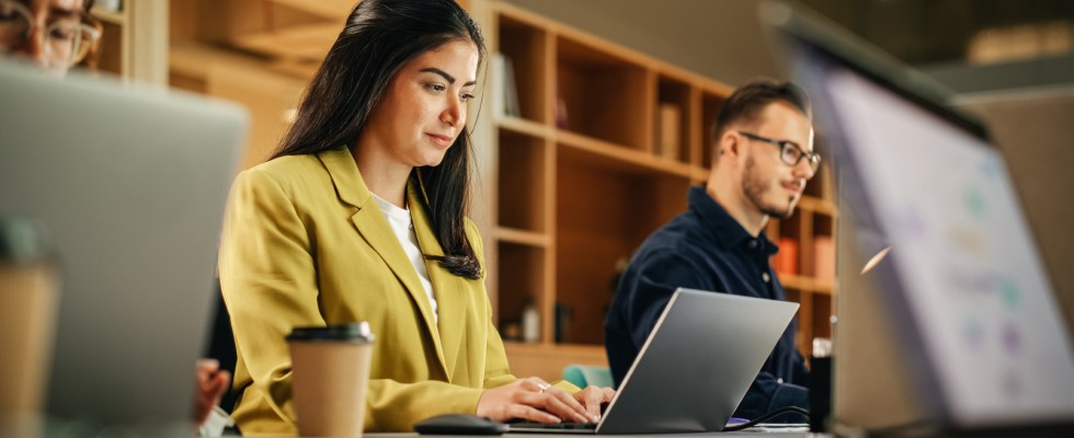 A diverse group of professionals collaborating on laptops in a modern office environment, focused and engaged in their tasks.