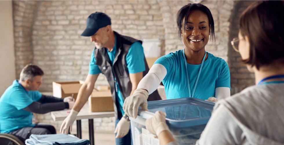 A woman in a blue shirt and gloves assists another woman with a box, showcasing teamwork and support.