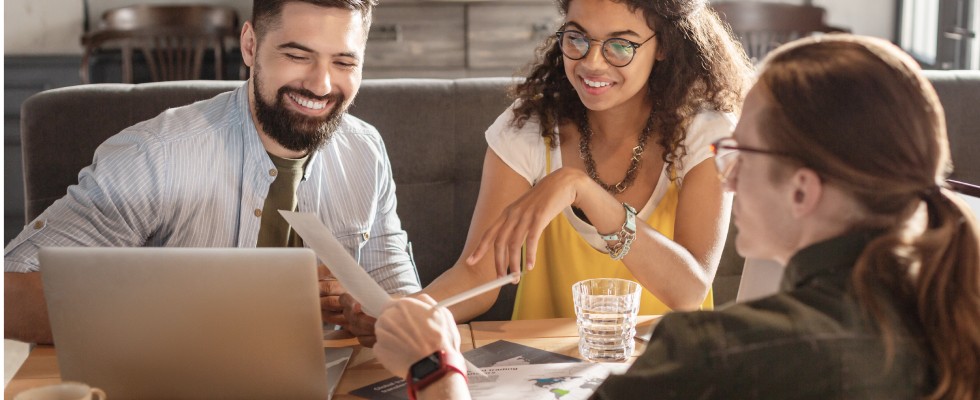 Three people sitting at desk and looking at paper
